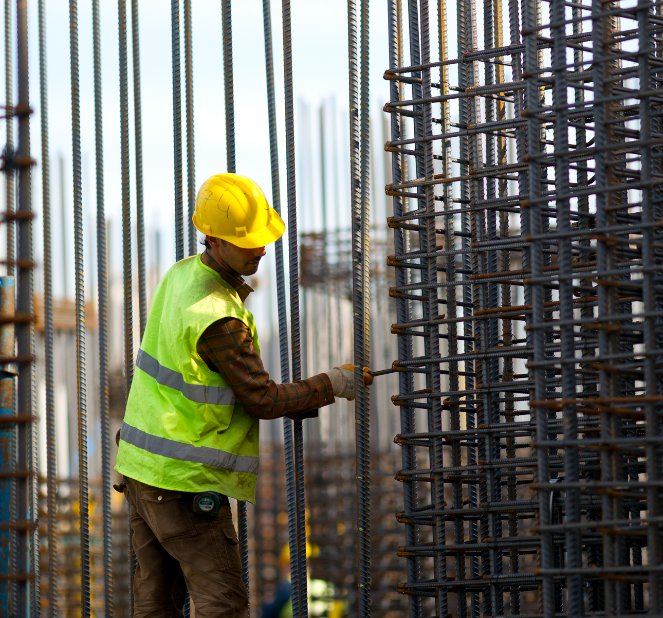 The builder in a construction vest and orange helmet standing against industrial background. Safety specialist, engineer, industry, architecture, manager, occupation, businessman, job concept