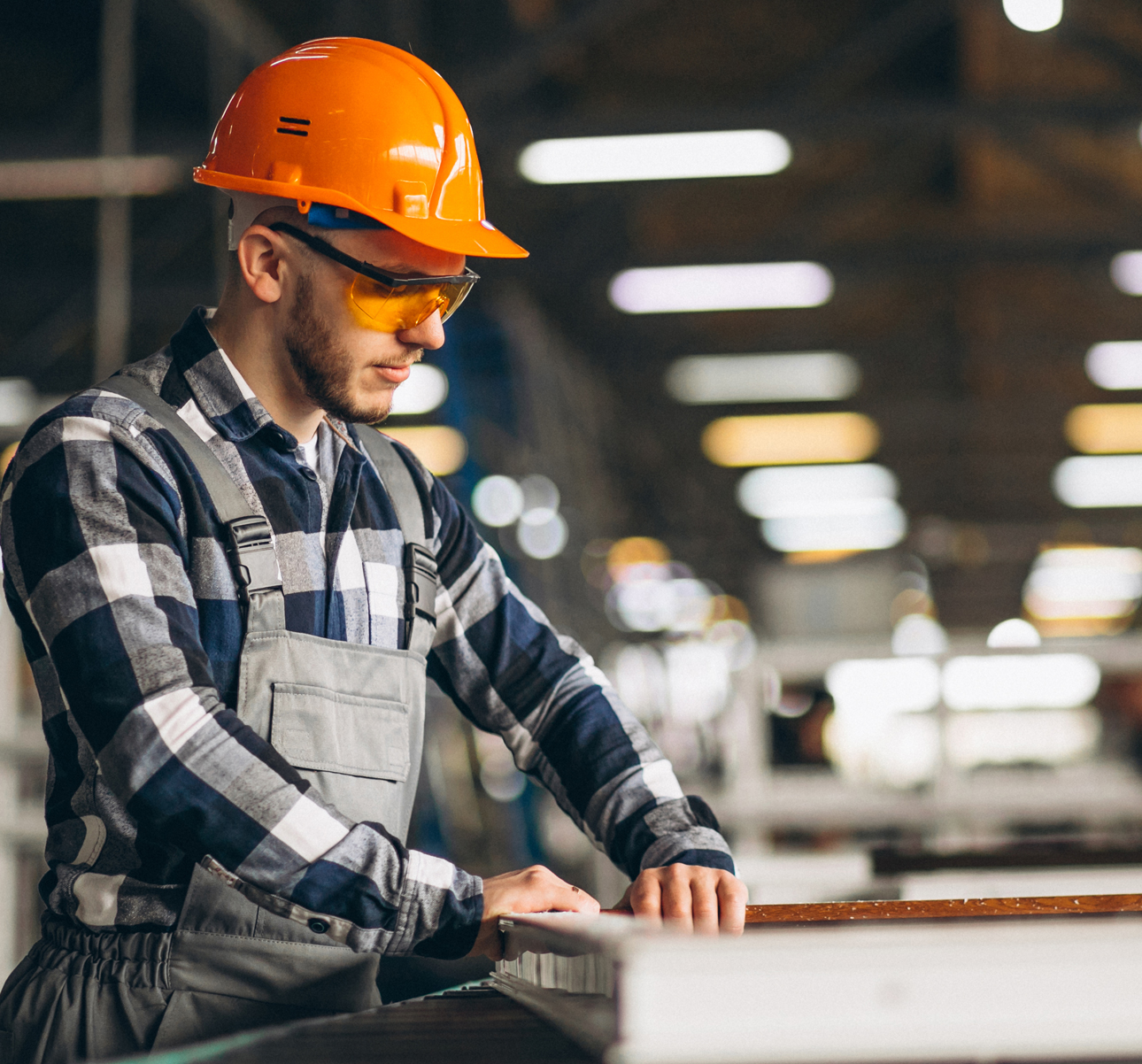 The builder in a construction vest and orange helmet standing against industrial background. Safety specialist, engineer, industry, architecture, manager, occupation, businessman, job concept